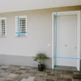 Misurazioni sul vano finestra e sulla porta d'ingresso. Due finestre con inferriate e una porta bianca su un muro beige.