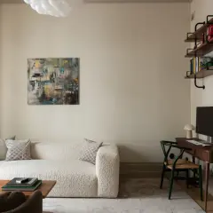 Soggiorno con divano bouclé bianco, tavolino in legno, quadro astratto e scrivania. Pareti color sabbia tortora chiaro RAL 1019.
