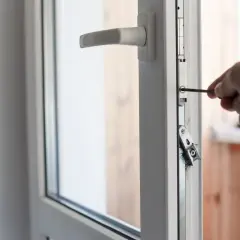 Mano con cacciavite effettua la regolazione cerniere finestre per un perfetto funzionamento.