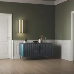 Interno con pareti verde salvia e boiserie bianca, porte bianche, un mobile blu e un pouf turchese.