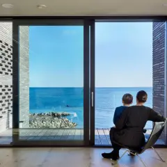 Madre e figlio osservano il mare da una stanza moderna, la luce naturale entra dalle ampie vetrate, illuminando l'ambiente.