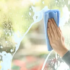 Mano pulisce un vetro macchiato con un panno blu, lasciando scie di schiuma.