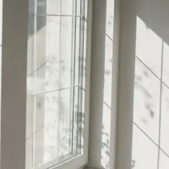 Luce solare intensa che crea ombre geometriche su una parete bianca e su un infisso in PVC, suggerendo che gli infissi in PVC si deformano al sole.