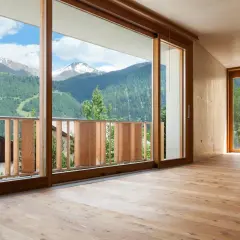 Interno con pavimento in legno e vista panoramica sulle montagne. L'arredamento con infissi marroni crea un'atmosfera calda e accogliente.