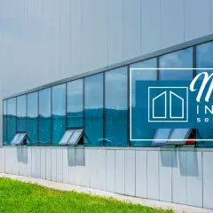 Edificio moderno con ampie vetrate riflettenti e infissi industriali. Logo "News Innova serramenti" sovrapposto.