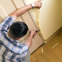 Uomo applica schiuma espansa per isolare porta ingresso dal freddo. Taglia l'eccesso per un lavoro pulito.