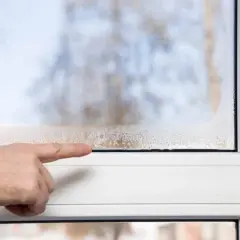 Dita che indica la condensa sulle finestre con doppi vetri, segno di umidità interna.