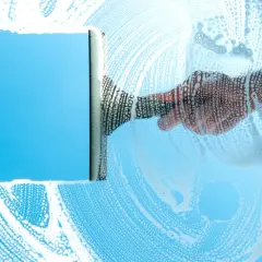 Mano con tergivetro crea strisce di schiuma su un vetro azzurro, per una perfetta pulizia finestre.