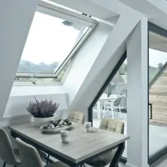 Tavolo da pranzo con sedie e una ciotola di frutta sotto un'apertura a bilico che lascia entrare la luce naturale.