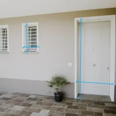Misurazioni sul vano finestra e sulla porta d'ingresso. Due finestre con inferriate e una porta bianca su un muro beige.