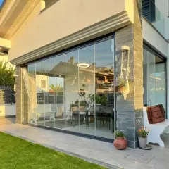 Moderna chiusura veranda in vetro, con arredi interni visibili. Un'elegante soluzione che rispetta la chiusura veranda normativa, valorizzando lo spazio esterno.