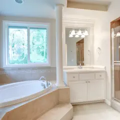 Ampia vasca da bagno sotto una finestra con vetri decorati, un bagno spazioso con doccia e lavandino.