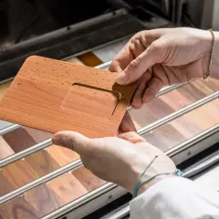 Mani che esaminano un campione di alluminio color legno, con una vasta gamma di finiture lignee in esposizione.