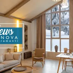 Interno accogliente con camino e divano, affacciato su un paesaggio innevato attraverso ampie finestre baita montagna.