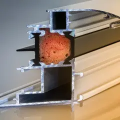 Sezione di un profilo per finestre: alluminio è un metallo leggero e resistente, con inserto isolante rosso e guarnizioni nere.