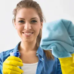 Donna sorridente con guanti gialli e panno blu, pronta a pulire le vetrate scorrevoli.