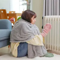 Ragazza avvolta in una coperta, con guanti rosa, vicino a un termosifone acceso, ma la casa è fredda nonostante i termosifoni.