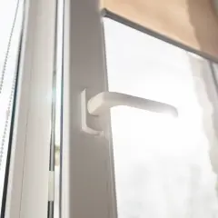 Maniglia finestra allentata, con catena per tende a rullo e luce solare che filtra.