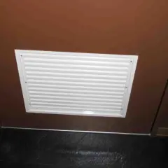 Griglia di ventilazione bianca su porta marrone, ideale per capire come arieggiare una stanza senza finestre.