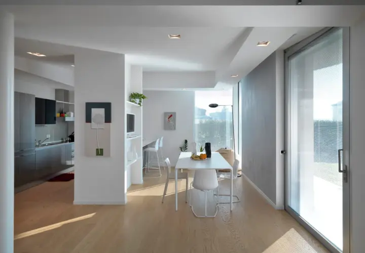 Interno moderno con cucina a vista, zona pranzo e un'ampia vetrata che sembra allargare una finestra in condominio, inondando di luce naturale.