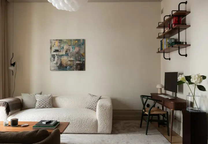 Soggiorno con divano bouclé bianco, tavolino in legno, quadro astratto e scrivania. Pareti color sabbia tortora chiaro RAL 1019.