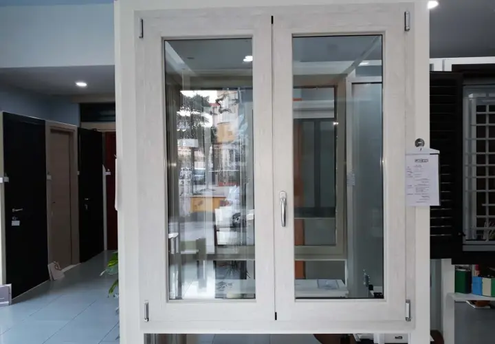 Finestra con telaio in alluminio effetto legno, con doppio vetro e maniglia argentata. Sullo sfondo, porte e altre finestre.