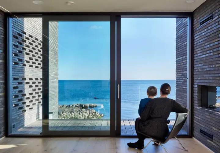 Madre e figlio osservano il mare da una stanza moderna, la luce naturale entra dalle ampie vetrate, illuminando l'ambiente.