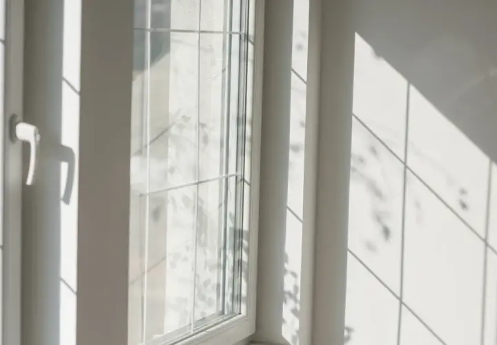 Luce solare intensa che crea ombre geometriche su una parete bianca e su un infisso in PVC, suggerendo che gli infissi in PVC si deformano al sole.