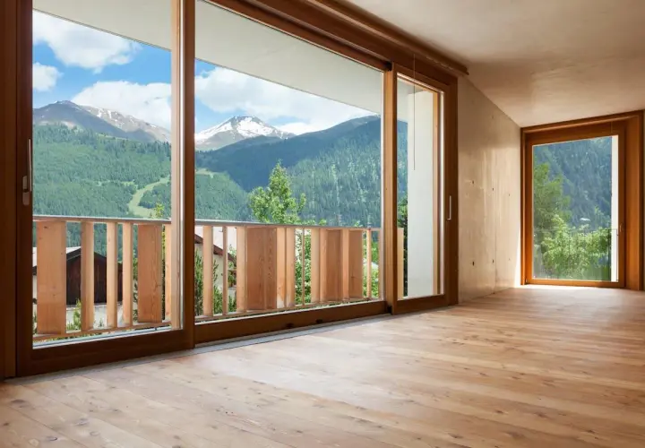 Interno con pavimento in legno e vista panoramica sulle montagne. L'arredamento con infissi marroni crea un'atmosfera calda e accogliente.
