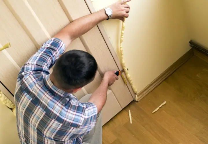 Uomo applica schiuma espansa per isolare porta ingresso dal freddo. Taglia l'eccesso per un lavoro pulito.