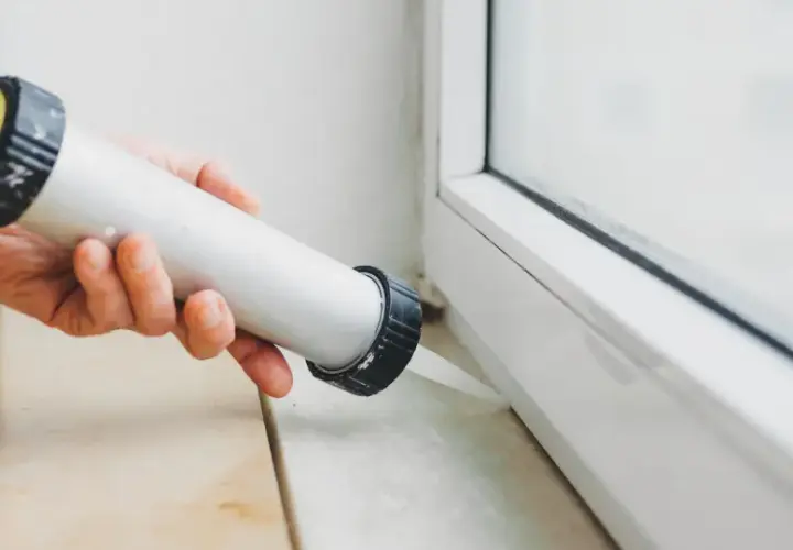 Applicazione di silicone per come isolare finestre vecchie in alluminio. Sigillatura del telaio per migliorare l'efficienza energetica.