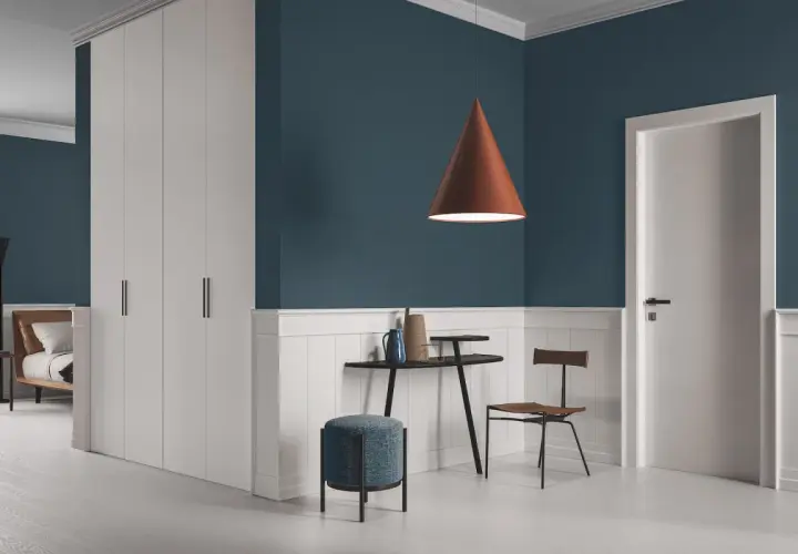Un soggiorno moderno con pareti blu intenso e battiscopa bianco. Un lampadario color terra e infissi marroni creano un contrasto caldo.