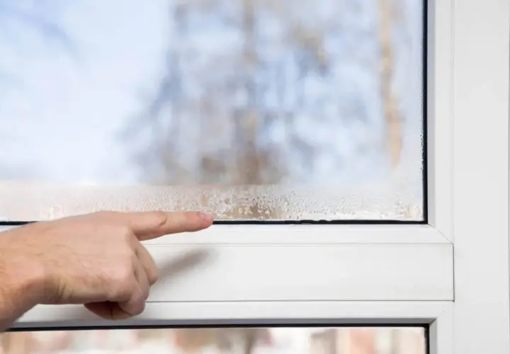 Dita che indica la condensa sulle finestre con doppi vetri, segno di umidità interna.