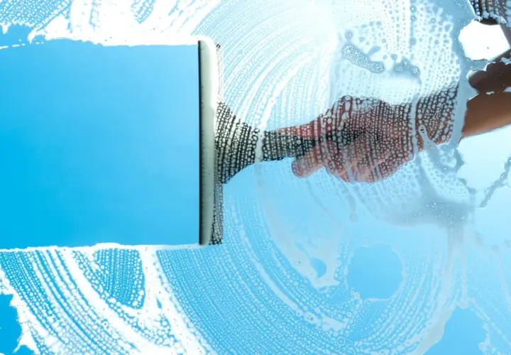 Mano con tergivetro crea strisce di schiuma su un vetro azzurro, per una perfetta pulizia finestre.