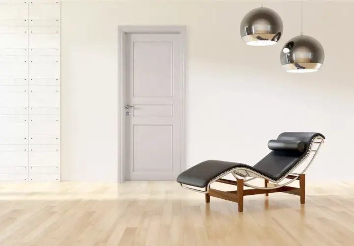 Un ambiente minimalista con porte bianche, pareti tortora, una chaise longue in pelle nera e due lampade a sospensione sferiche.