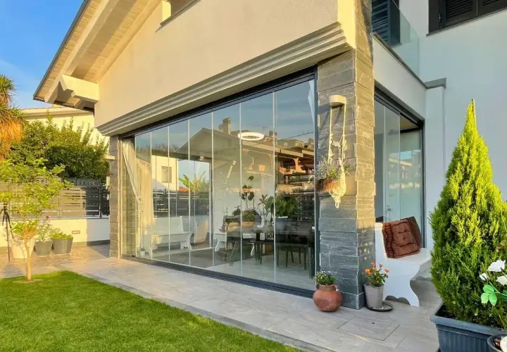 Moderna chiusura veranda in vetro, con arredi interni visibili. Un'elegante soluzione che rispetta la chiusura veranda normativa, valorizzando lo spazio esterno.