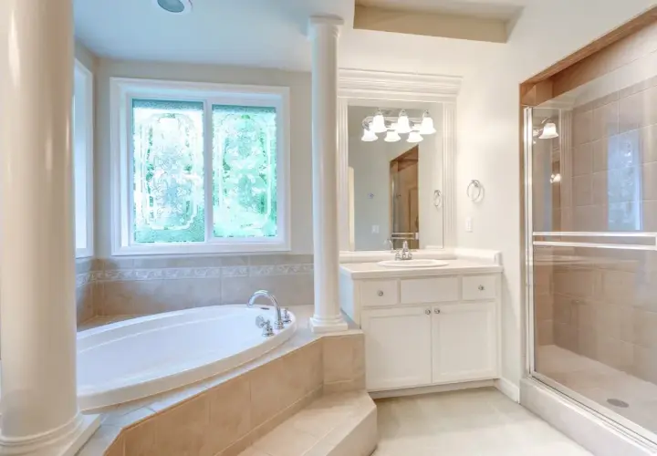 Ampia vasca da bagno sotto una finestra con vetri decorati, un bagno spazioso con doccia e lavandino.