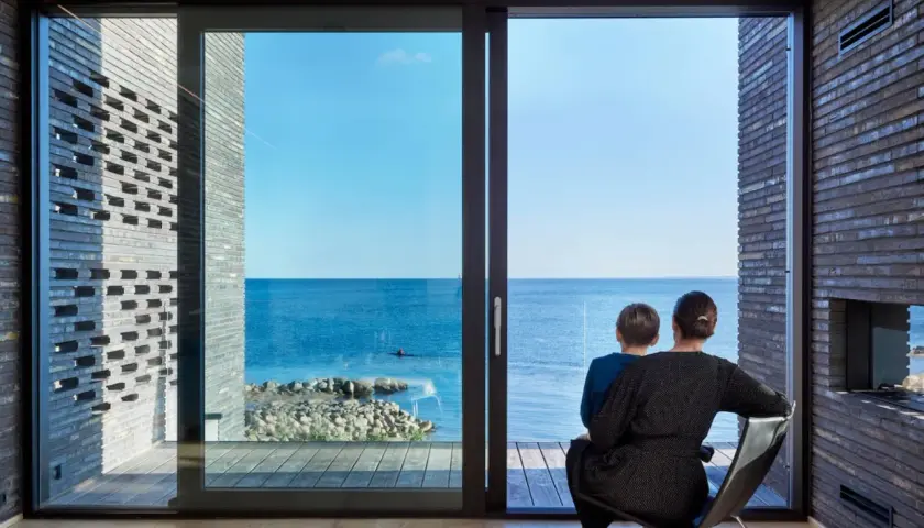 Madre e figlio osservano il mare da una stanza moderna, la luce naturale entra dalle ampie vetrate, illuminando l'ambiente.