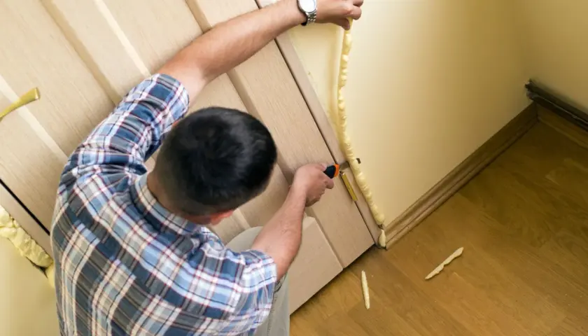 Uomo applica schiuma espansa per isolare porta ingresso dal freddo. Taglia l'eccesso per un lavoro pulito.