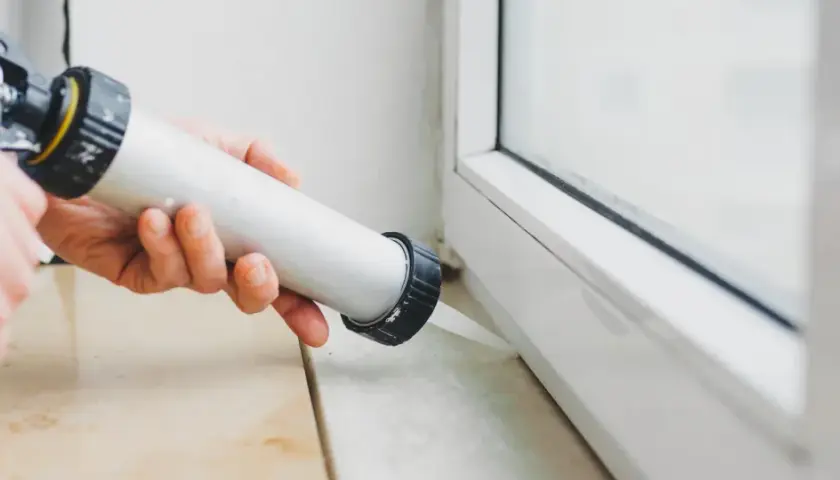 Applicazione di silicone per come isolare finestre vecchie in alluminio. Sigillatura del telaio per migliorare l'efficienza energetica.