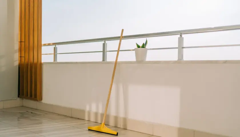 Scopa gialla appoggiata sul pavimento piastrellato, pronta per pulire la veranda del balcone.