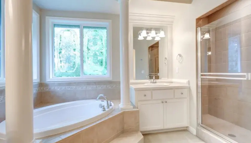 Ampia vasca da bagno sotto una finestra con vetri decorati, un bagno spazioso con doccia e lavandino.