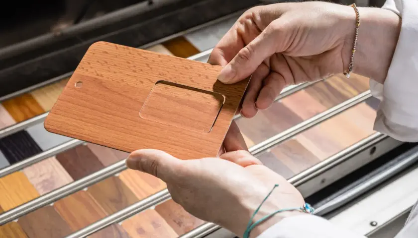 Mani che esaminano un campione di alluminio color legno, con una vasta gamma di finiture lignee in esposizione.