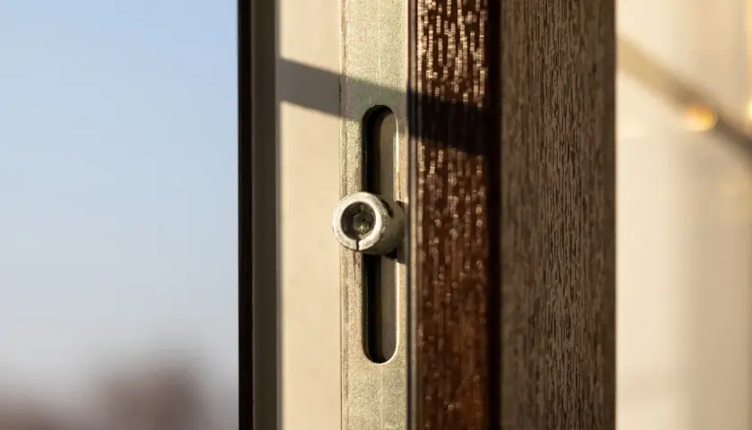 Dettaglio di un infisso con meccanismo per microventilazione. La luce del sole illumina il profilo scuro e la ferramenta metallica.