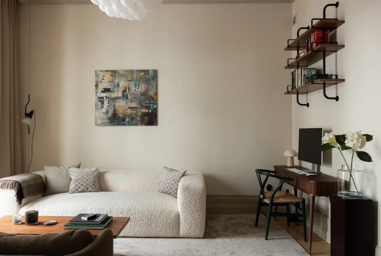 Soggiorno con divano bouclé bianco, tavolino in legno, quadro astratto e scrivania. Pareti color sabbia tortora chiaro RAL 1019.