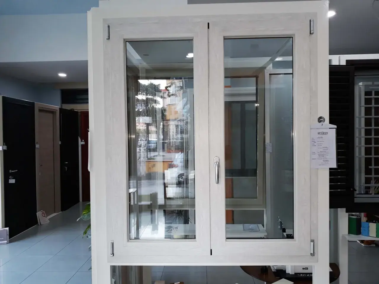 Finestra con telaio in alluminio effetto legno, con doppio vetro e maniglia argentata. Sullo sfondo, porte e altre finestre.