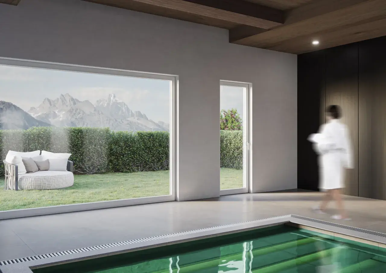 Interno moderno con piscina, grandi vetrate che incorniciano montagne e giardino, e infissi in legno lamellare che creano un'atmosfera calda.
