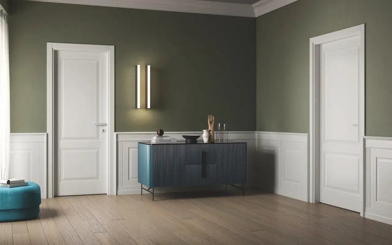 Interno con pareti verde salvia e boiserie bianca, porte bianche, un mobile blu e un pouf turchese.