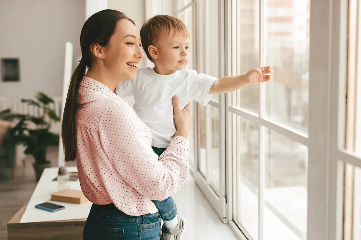 Mamma e bambino guardano fuori dalla finestra. Un giorno, potremo rifare gli infissi a costo zero e godere di una vista ancora più bella.