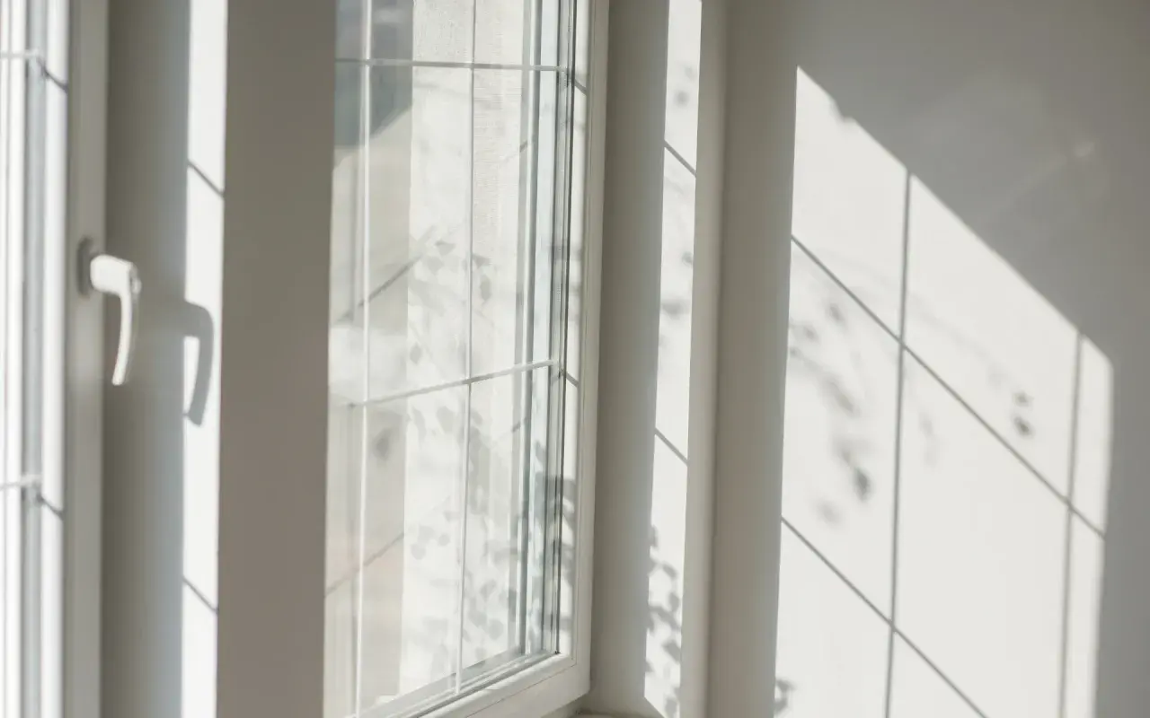 Luce solare intensa che crea ombre geometriche su una parete bianca e su un infisso in PVC, suggerendo che gli infissi in PVC si deformano al sole.